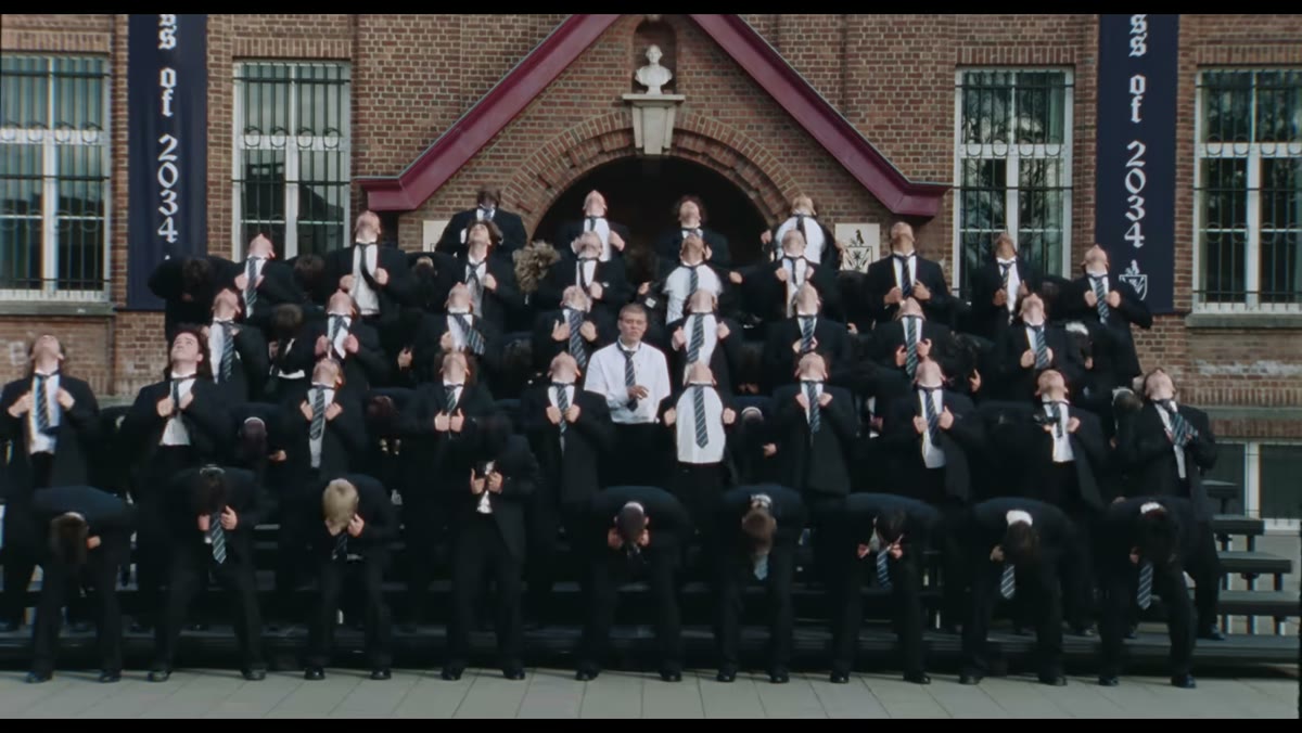 A crowd in school uniforms dancing in unison on the steps in front of a school building in GENER8ION's STORM music video; the STORM AI trend replaces the center dancer or the whole crowd. Source: GENER8ION official YouTube (2026)